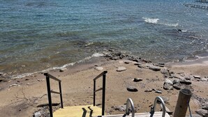 A wooden deck leading to a rocky beach with clear water and distant land.