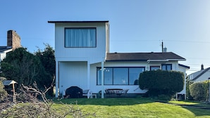 Une maison moderne à deux étages, dotée d’un grand garage, d’un coin repas avec mobilier d’extérieur et d’une pelouse bien entretenue.