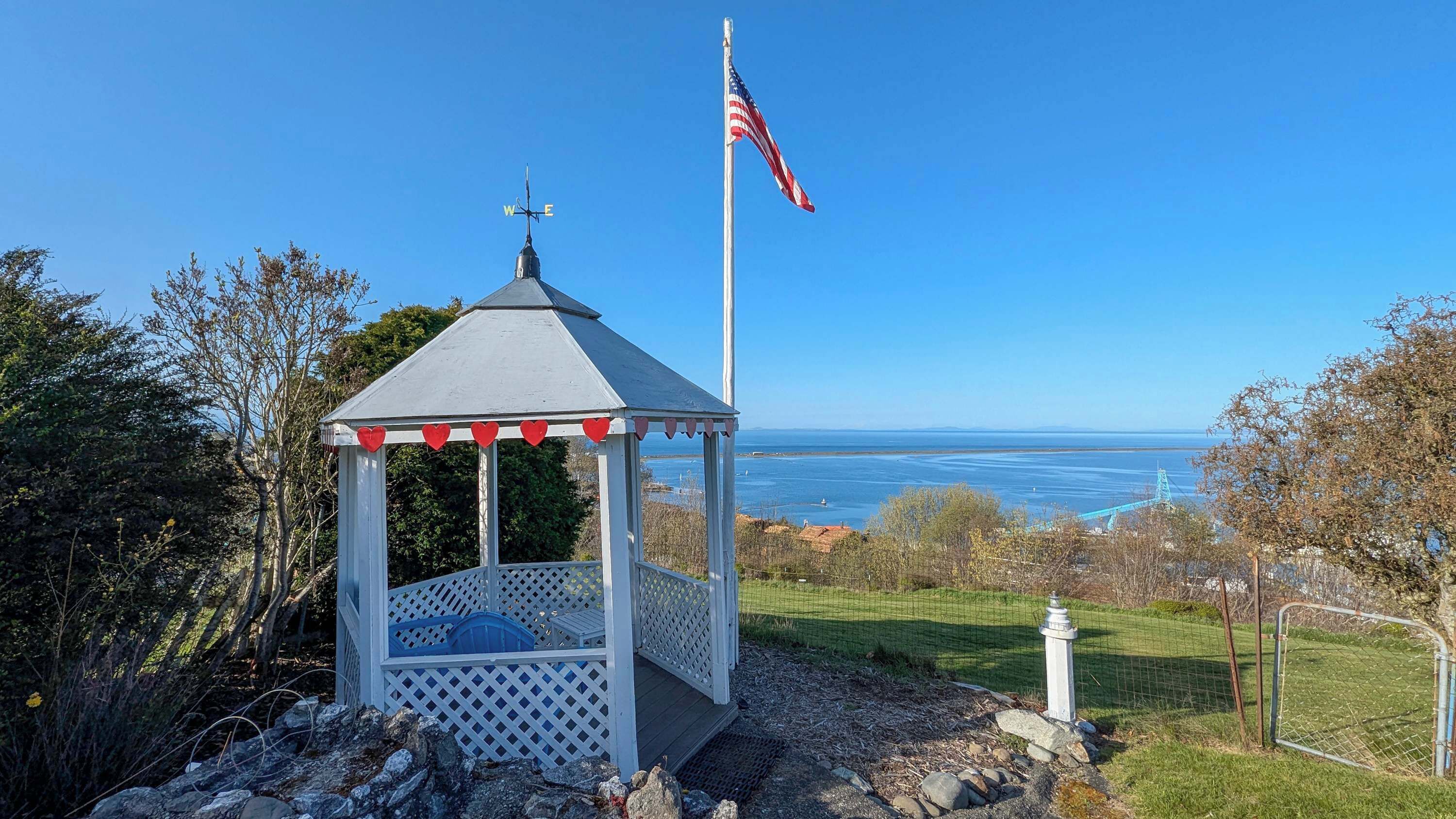 A gazebo with a flagpole, overlooking a body of water.
