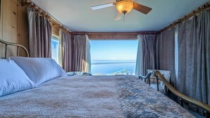 Une chambre avec un grand lit, un ventilateur de plafond et une vue sur un pont et sur l’eau.