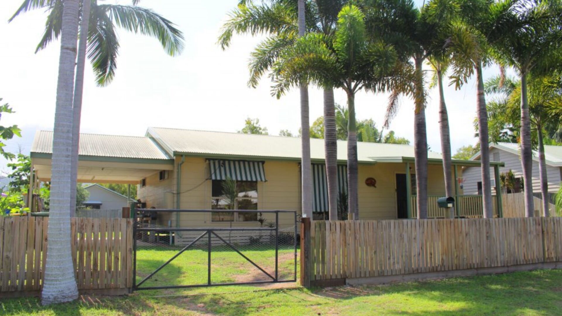 A single-story house with a fenced yard, surrounded by palm trees.