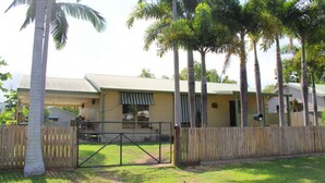 A single-story house with a fenced yard, surrounded by palm trees.