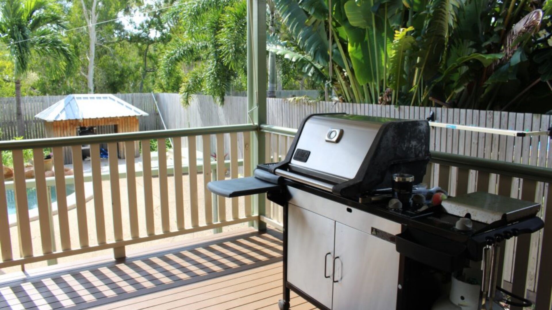 A covered outdoor area with a barbecue grill, wooden deck, and a wooden fence.