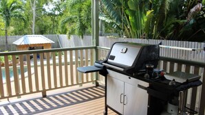 A covered outdoor area with a barbecue grill, wooden deck, and a wooden fence.