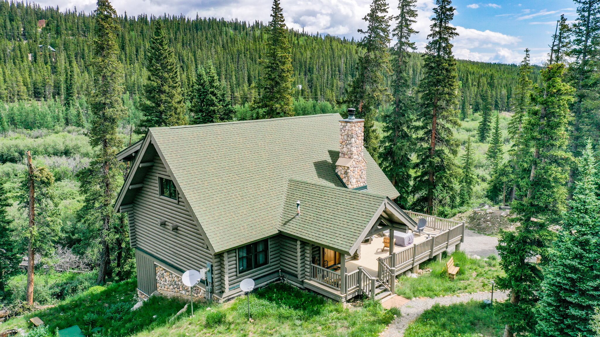 A log cabin with a stone chimney, surrounded by dense forest.