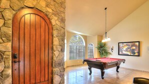 A wooden door with a stone archway, a pool table, and a billiards cue rack in a room with tiled flooring and a large window. - Arrowhead (Glendale)