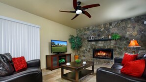 A living room with a stone fireplace, leather sofas, a coffee table, and a television. - Arrowhead (Glendale)