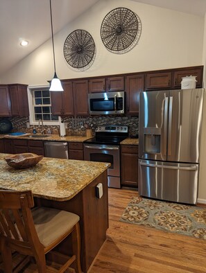 A modern kitchen with granite countertops, stainless steel appliances, wooden cabinets, and a large island with bar stools. - Dog Friendly Skyline Drive Retreat: 3 King Suites, Views & Firepit! 1pm checkout (Front Royal)
