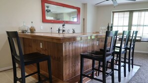 Une cuisine avec un bar et des chaises en bois, un miroir à cadre rouge et une fenêtre avec des stores.