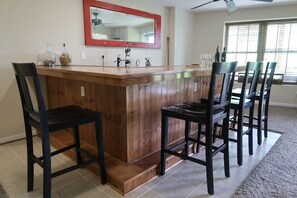 A kitchen with a wooden bar and chairs, a red-framed mirror, and a window with blinds.
