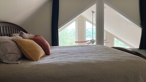 Un lit avec une tête de lit, des oreillers et une vue sur l’extérieur par une fenêtre.