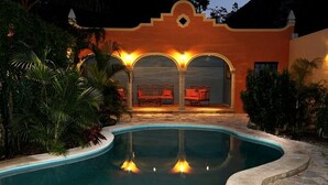A swimming pool with a curved edge, surrounded by lush greenery and a building with arches and a balcony. - Tranquil Tropical Oasis in the Historic Center/ Full Size Pool (Merida)