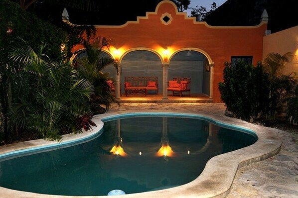 A swimming pool with a curved edge, surrounded by lush greenery and a building with arches and a balcony. - Tranquil Tropical Oasis in the Historic Center/ Full Size Pool (Merida)