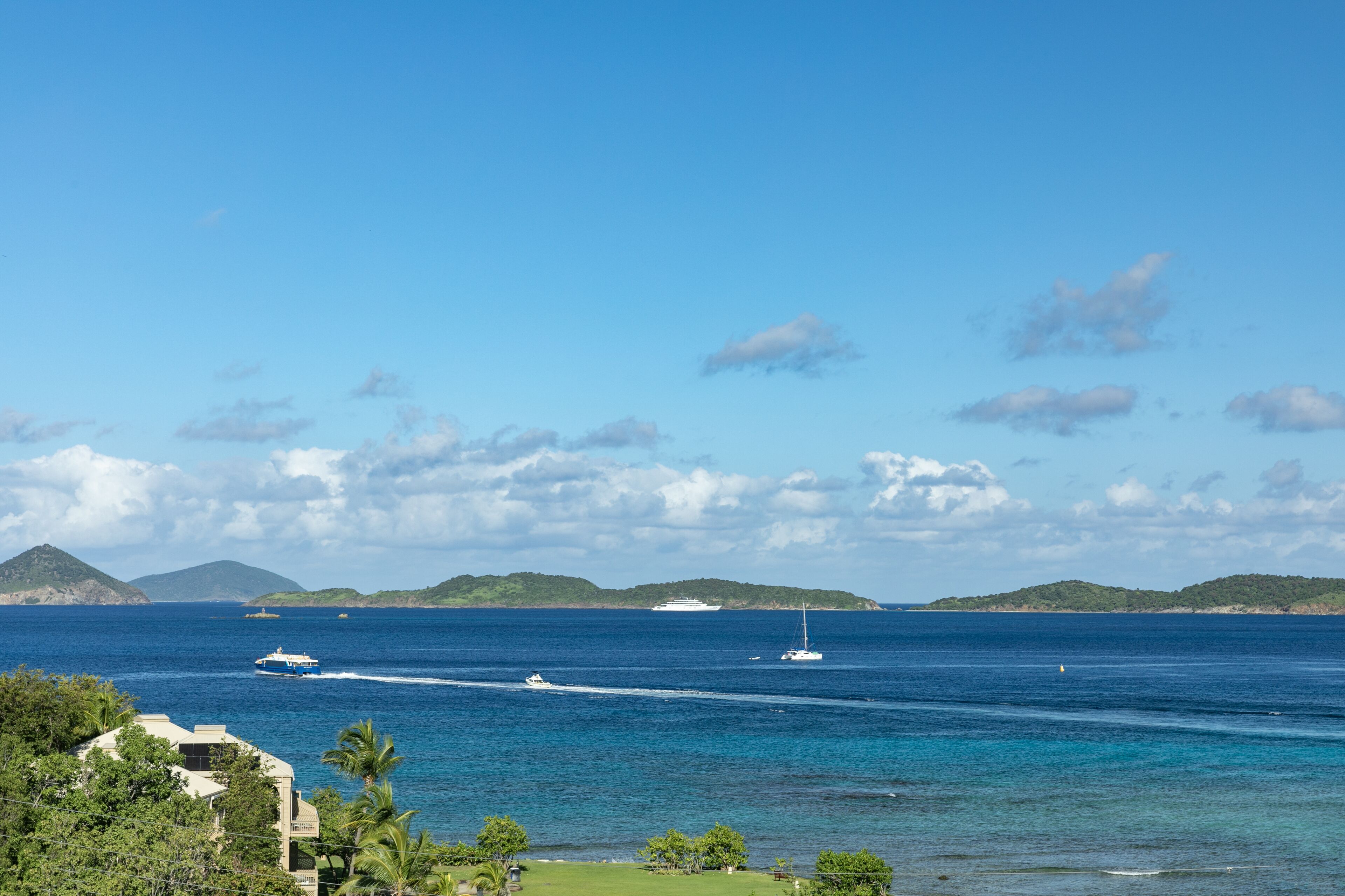 A coastal view with a clear sky, a yacht, and a cruise ship in the distance.