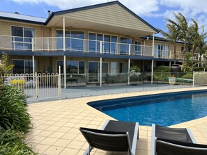 A two-story building with a swimming pool, outdoor seating, and a fenced patio area.
