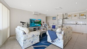A modern living room with a flat-screen TV, two patterned sofas, a coffee table, and a blue rug. - Resort Style Apartment (Ground Floor) - Pool & More. Pets Welcome. (Lakes Entrance)