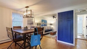 A dining area with a wooden table and chairs, a chandelier, and a blue door in the background. - Quintessential Cottage near beaches and Newport center. (Middletown)