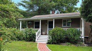 A house with a covered porch, a brick pathway leading to the entrance, and lush greenery surrounding the property. - Quintessential Cottage near beaches and Newport center. (Middletown)