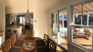 Un comedor con una mesa dispuesta para cuatro, una cocina al fondo y vistas a una terraza de madera.