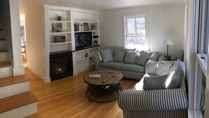Una sala de estar con chimenea, sofá a rayas y una estantería.