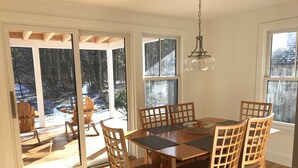 Comedor con mesa y sillas de madera, ventanas amplias y vistas a una terraza nevada.