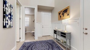A hallway with a patterned rug, a world map, and a lamp on a console table.