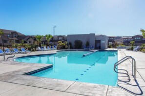 A swimming pool with blue tiles, surrounded by lounge chairs and a small building.