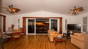 Una sala de estar amplia con suelo de madera, comedor con mesa y sillas, sofá, televisor y ventilador de techo.