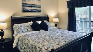 Een slaapkamer met een bed, twee bedlampen, een plafondventilator, een raam met gordijnen en een schilderij aan de muur.