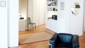 Amplia habitación con techo de madera, un sillón de cuero negro, una estantería y una puerta con un espejo redondo.