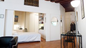 Una habitación de hotel con cama, escritorio con sillas, armario y perchero.
