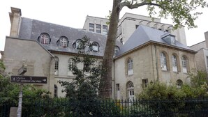 Un edificio histórico con fachada de piedra, múltiples ventanas y un cartel que indica indicaciones hacia lugares cercanos.