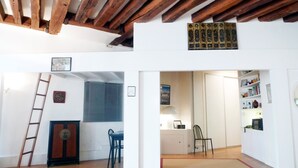 Una habitación con vigas de madera en el techo, un escritorio con una silla, una estantería y una puerta que da a otra habitación.