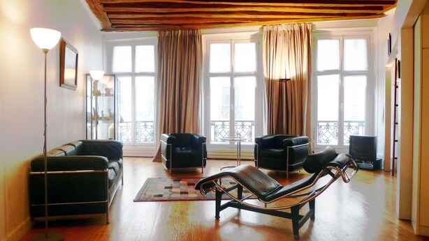 Una sala de estar con techo de madera, dos sofás de cuero negro, un sillón reclinable negro, una lámpara de pie y un televisor.