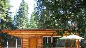 A wooden cabin with a large window, a door, and a patio area with a table and chairs. - MODERN LOG CABIN-HOT TUB-TAHOE PARK BCH ACCESS (Tahoe City)