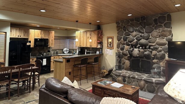 A cozy living area with a stone fireplace, wooden ceiling, and a kitchen with wooden cabinets. - MODERN LOG CABIN-HOT TUB-TAHOE PARK BCH ACCESS (Tahoe City)