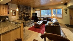 A spacious living area with a stone fireplace, a large window, and a cozy seating arrangement. - MODERN LOG CABIN-HOT TUB-TAHOE PARK BCH ACCESS (Tahoe City)