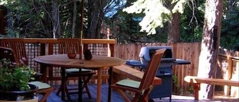 An outdoor deck with a table, chairs, a grill, and an umbrella.