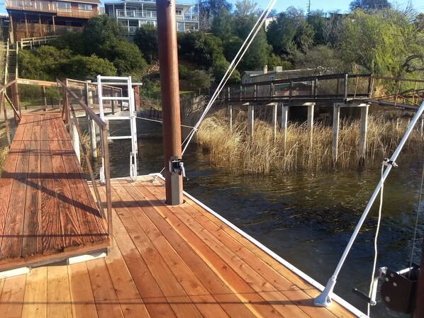 A wooden deck with a metal railing overlooking a body of water, surrounded by vegetation and buildings. - Beautiful Lake Front house with Spectacular view, new deck/private dock sleep 6 (Clearlake)