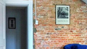 Una habitación con paredes de ladrillo visto, una silla azul, un tapete estampado y un cuadro enmarcado de Central Park.