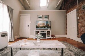 Una sala de estar con televisor de pantalla plana, un mueble blanco para equipo electrónico, una mesa de piedra y una pared de ladrillo.
