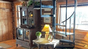 A rustic cabin interior with a wooden staircase, a cabinet with glass doors, a small table with a lamp, and a leather couch. - Charming Log Cabin on Private Pond Nestled in Woods Near Holiday Valley Resort 
 (Great Valley)