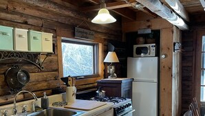 A rustic kitchen with wooden beams, a stove, sink, and cabinets. - Charming Log Cabin on Private Pond Nestled in Woods Near Holiday Valley Resort 
 (Great Valley)