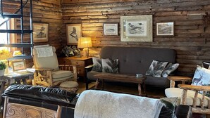 A rustic cabin interior with a wooden ceiling, a sofa, a dining table with chairs, and framed pictures on the walls. - Charming Log Cabin on Private Pond Nestled in Woods Near Holiday Valley Resort 
 (Great Valley)