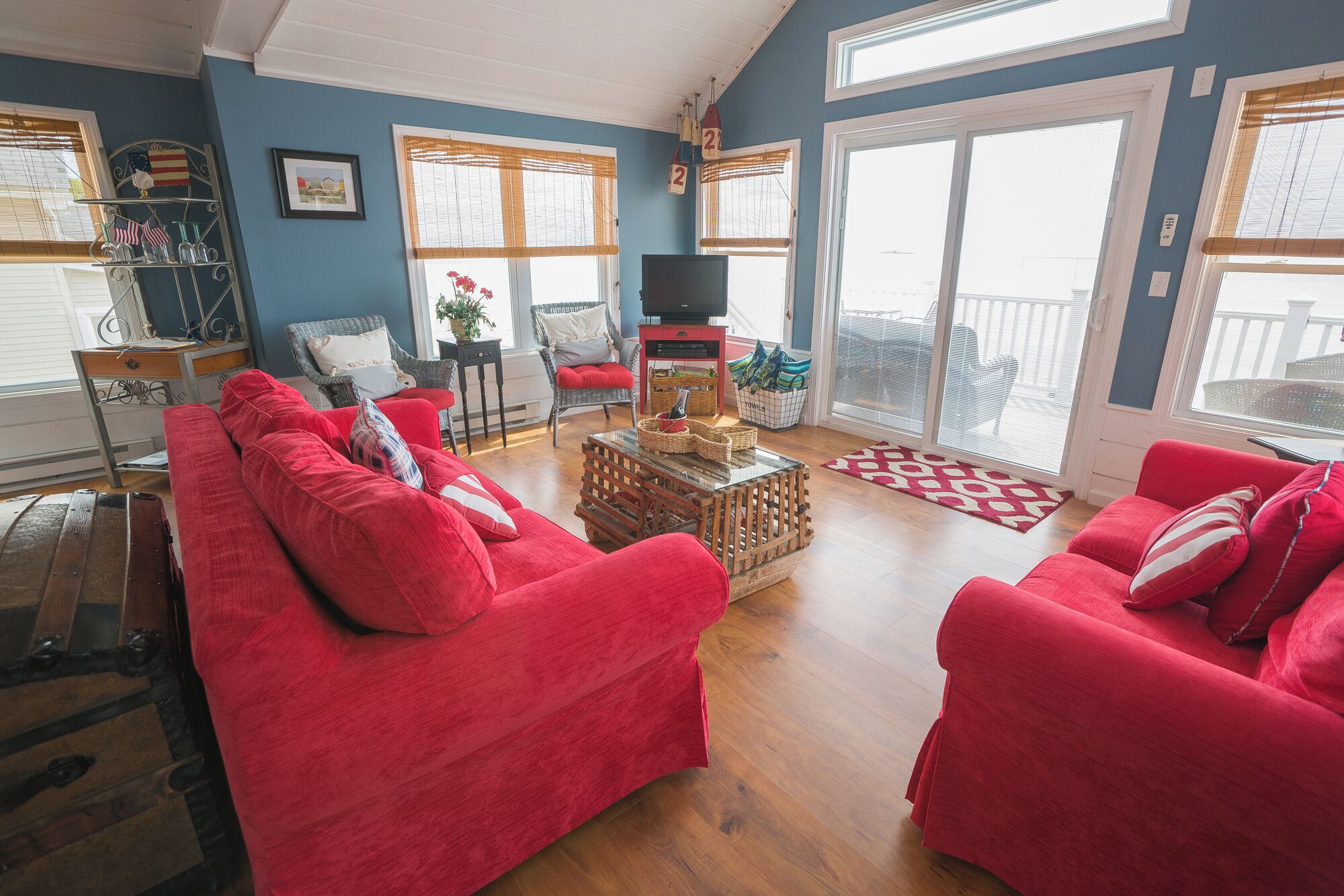 A living room with red sofas, a wooden coffee table, wicker baskets, and a TV on a stand.
