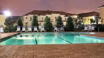 A swimming pool with lounge chairs and a fence, surrounded by buildings with a tiled roof.