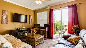 A living room with a sofa, a coffee table, a TV, and a balcony with red curtains.