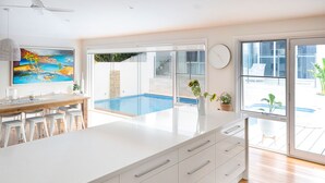 Et moderne køkken med en stor ø, et spiseområde med barstole, udsigt til en swimmingpool og et stort vindue.