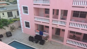 Un immeuble rose à plusieurs étages, doté de balcons, d’une piscine et d’un espace extérieur aménagé pour s’asseoir.