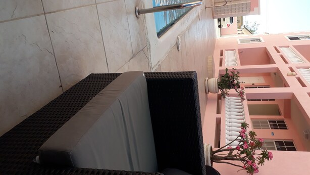 Un espace extérieur carrelé avec une piscine, un fauteuil de relaxation et un bâtiment doté de balcons.